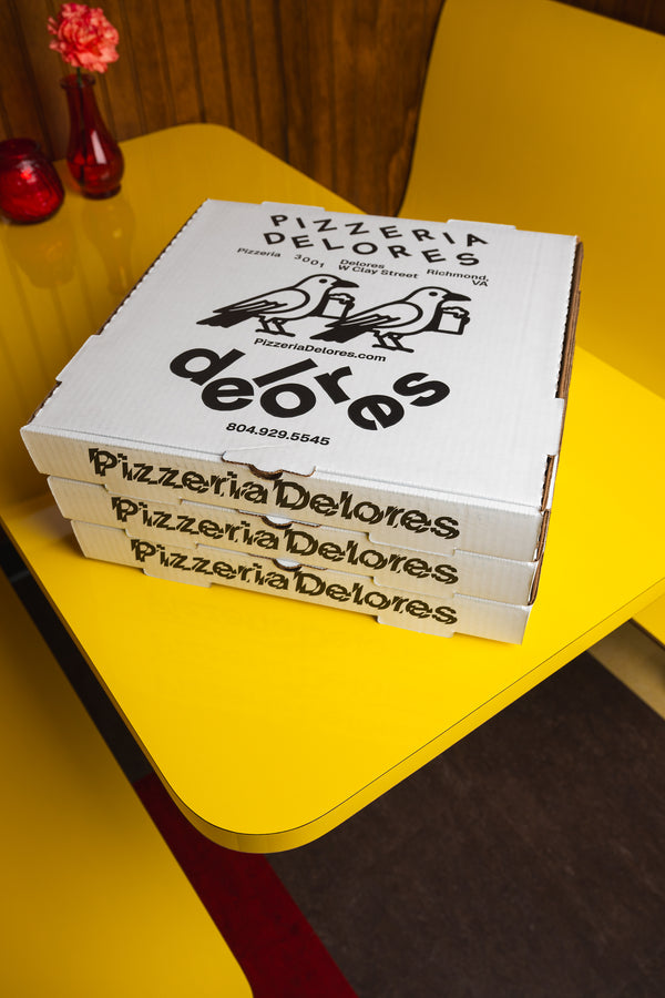Stack of Pizzeria Delores pizza boxes on a yellow table