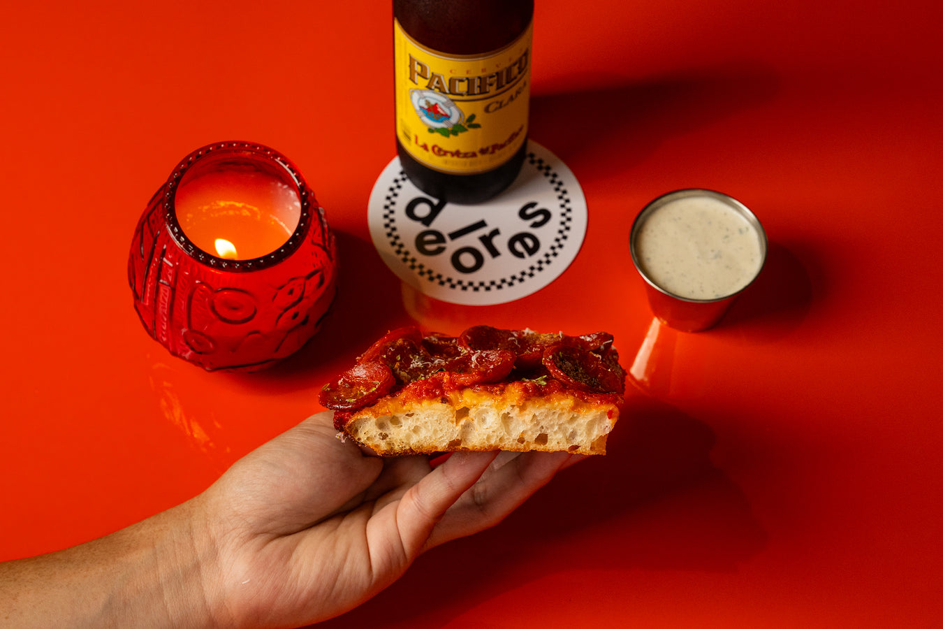 Hand holding a pepperoni square with a beer and ranch